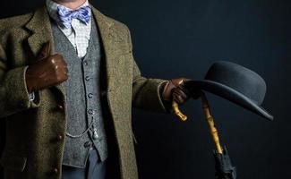 porträtt av elegant engelsk herre i tweed kostym innehav paraply och kastare hatt. årgång stil och retro mode av brittiskt herre. foto