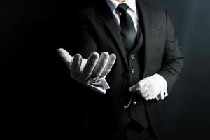 porträtt av vänlig butler i mörk kostym och vit handskar förlängning en portion hand. begrepp av professionell gästfrihet och vänlighet. foto