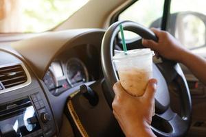 närbild hand håll kopp av iced kaffe till dryck i bil. begrepp, baverge för uppfriskande eller portion till vaken från sovande under körning den där kan orsak bil olycka. foto