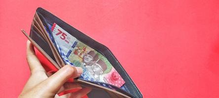 en man innehar en plånbok som innehåller de senast utgåva av indonesiska sedlar. foto