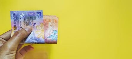 man innehav indonesiska rupiah sedlar de senast utgåva, isolerat på en gul bakgrund och negativ Plats. foto