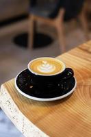 svart kopp av kaffe med grädde, cappuccino med en mönster närbild står på en trä- tabell foto