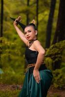 asiatisk kvinna innehav henne svart hår i en grön kostym medan bär smink och Framställ i främre av de skog under de dansa festival foto