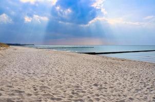 Sol strålar glans genom tät moln på de strand av de baltic hav. groynes på de kust foto