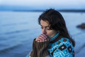 en flicka i en skön Tröja i höst på de hav strand värms upp henne kall händer med henne andetag, de kustlinje, svalka foto