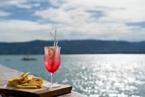 en glas av juice eller en cocktail med en tallrik av franska frites för lunch i en skön hav se. havet restaurang med ljus solsken göra Lycklig i Semester. foto