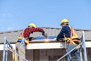 en team av asiatisk tekniker installerar sol- paneler på de tak av en hus. tvärsnitt se av byggare i hjälm montera sol- panel systemet begrepp av förnybar energi foto