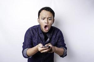 chockade asiatisk man bär blå skjorta och innehav hans telefon, isolerat förbi vit bakgrund foto