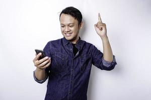 en porträtt av en Lycklig asiatisk man bär en blå skjorta och innehav henne telefon, isolerat förbi vit bakgrund foto