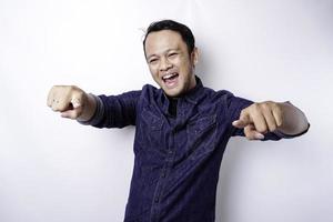 ung asiatisk man bär blå skjorta stående över isolerat vit bakgrund pekande fingrar till kamera med Lycklig ansikte. Bra energi och vibrafon. foto