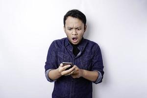 chockade asiatisk man bär blå skjorta och innehav hans telefon, isolerat förbi vit bakgrund foto