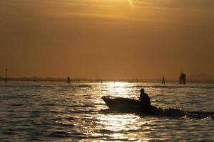 fiskare silhuett på solnedgång i Venedig lagun chioggia hamn från en båt foto