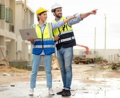 ingenjör man och kvinna arkitekt ha på sig säkerhet hjälmar diskutera hus utveckling projekt på konstruktion webbplats använder sig av bärbar dator dator. entreprenör chef granskning byggnad egendom infrastruktur. foto