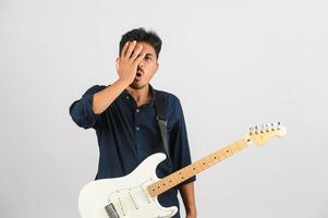 porträtt av ung asiatisk man i blå skjorta med elektronisk gitarr isolerat på vit bakgrund foto