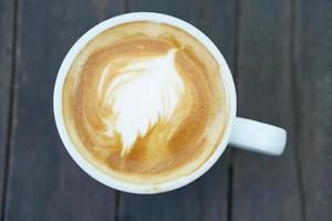 varm kaffe med blommig skum i en vit kopp grå trä bakgrund foto