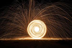 spinning och brinnande stål ull gnistra brand i de cirkel form med lång hastighet slutare skjuta lysande ljus linje till de jord. foto