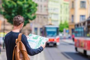 ung man med en stad Karta och ryggsäck i Europa. caucasian turist ser på de Karta av europeisk stad i Sök av attraktioner. foto