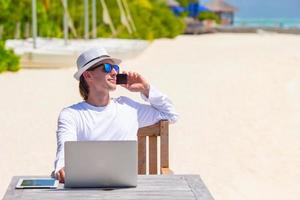 ung man med läsplatta dator och cell telefon på tropisk strand foto