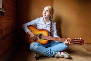 ung hipster kvinna Sammanträde på golv och spelar gitarr på Hem. tonåring flicka inlärning till spela låt och skrivning musik i henne rum. hobby, livsstil, koppla av, instrument, fritid, utbildning begrepp. foto