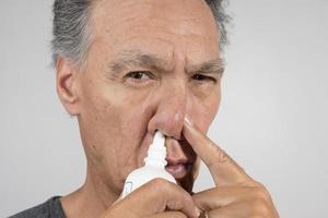 senior man använder sig av en nasal spray för hans torr näsa foto