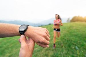 atletisk tränare innehar de stoppur medan Träning en flicka löpning i natur foto