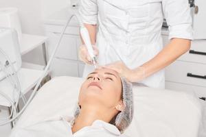 kosmetolog gör aqua exfoliering för föryngring kvinna ansikte hudvård, procedur i skönhet salong foto
