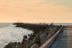 lång fotgängare pir med människor gående på solnedgång i Europa, betong vågbrytare och blå lugna hav foto