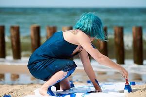 begåvad blåhårig kvinna prestanda konstnär insmord med gouache målarfärger på stor duk på strand foto