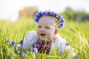 en Lycklig liten flicka i nationell vitryska eller ukrainska kläder lögner på de gräs och skrattar. skön slavic barn. en liten bebis i ett broderad skjorta upp till en år gammal på en sommar äng. foto