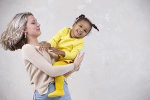 multietnisk mamma och dotter spela på Hem. glad mor med liten dotter av afrikansk nationalitet. familj från annorlunda lopp. foto