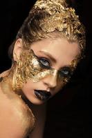 närbild porträtt av skön ung kvinna med gyllene folie på ansikte. kreativ gyllene smink på svart bakgrund foto