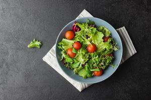 grön sallad löv med körsbär tomater i skål på svart tabell. foto