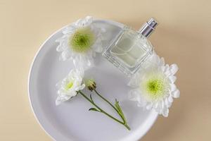 ett elegant flaska med en kosmetisk, parfym eller spray på en vit keramisk tallrik bland vit blommor. topp se. en tom layout. foto