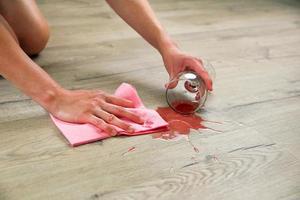 glas av röd vin föll på laminera, vin spillts på golv. en kvinna våtservetter de laminera från fukt. foto