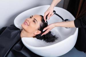 professionell frisör tvättning hår av ung kvinna i skönhet salong foto