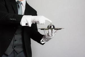 porträtt av butler eller concierge i formell klädsel och vit handskar innehav klocka på silver- tjänande bricka. service industri och professionell gästfrihet. foto