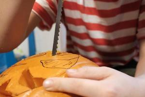 halloween förberedelse. barn i en randig t-shirt träsnideri pumpa in i Pumpalykta medan Sammanträde på de golv, i de hus. foto