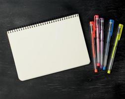 öppen anteckningsbok och gel penna på en svart trä- bakgrund foto