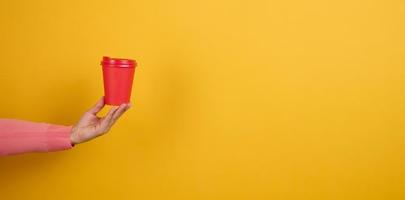 hand innehar papper kartong röd kopp för kaffe, gul bakgrund. miljövänlig servis, kopia Plats foto