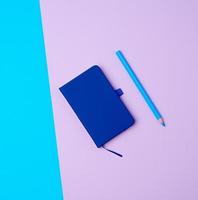 stängd anteckningsbok och trä- blå penna på en färgad bakgrund, topp se foto