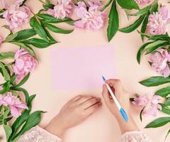 kvinna hand innehar hand en vit penna över tömma rosa ark av papper foto