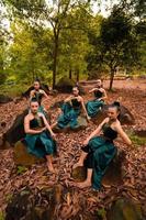 en grupp av indonesiska dansare Sammanträde underbart på de sten med brun löv i de bakgrund inuti de skog foto