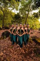 en bred skott av ett asiatisk kvinna stående tillsammans i de skog medan bär en grön dansa kostym med död- löv foto