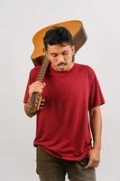 porträtt av ung asiatisk man i röd t-shirt bärande ett akustisk gitarr isolerat på vit bakgrund foto