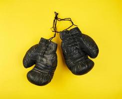 par av svart läder mycket gammal boxning handskar på en gul bakgrund foto