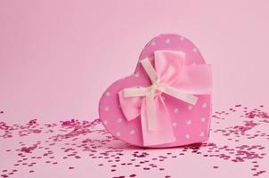 stängd rosa gåva låda i de form av en hjärta med en rosett på en rosa bakgrund foto