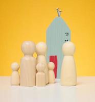 trä- hus och miniatyr- figurer av en familj och en fastighetsmäklare på en gul bakgrund. foto