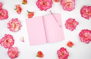 öppen anteckningsbok med rosa tom sidor på en vit bakgrund och kronblad av en rosa ro foto