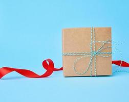 fyrkant brun kartong låda för en gåva och vriden silke röd band foto