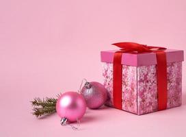 rosa gåva låda med rosett, grön gran gren och två dekorativ rosa bollar foto